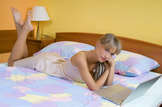 pretty young woman laying down on bed with a laptop looking in camera