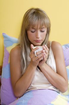 young woman between colored sheet drinking a cup of tea before to sleep