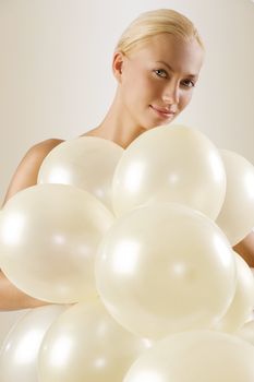 beautiful blond woman playing with white balloons and looking in camera smiling