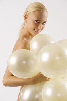 beautiful blond woman arming and cocoverin her body with white balloons looking in camera