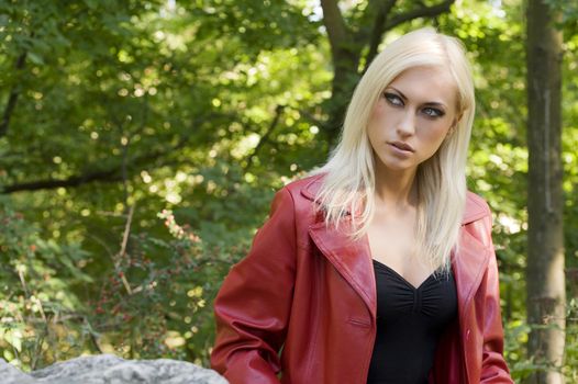 Closeup portrait of a sensual blond girl with red coat outside in a park