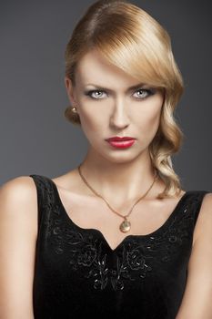 young elegant blond woman wearing black dress with an old fashion hairtyle and necklace jewellery, she is in front of the camera and looks in to the lens