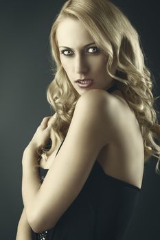 elegant and sexy woman in black with shorts and with a curly hair style over black background, she is turned of three quarters at right, looks in to the lens with aggressive expression, her left hand is on the right shoulder