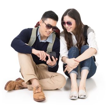 Asian young couple traveling and sitting on ground and using mobile phone, full length portrait on white background.