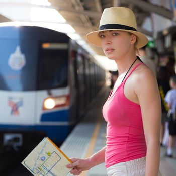 Young woman with a map in her hand waiting on the platform of a railway station for their train. to arrive.