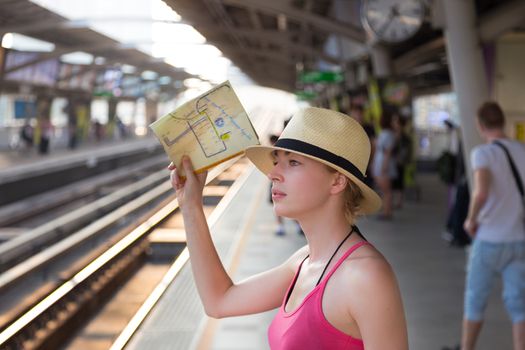 Young woman with a map in her hand waiting on the platform of a railway station for their train. to arrive.