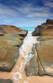 The ocean washes through a rock crevice.  Soldiers Beach, NSW, Australia.  Nice motion in the water contrasts the steadfastness of the rocks.