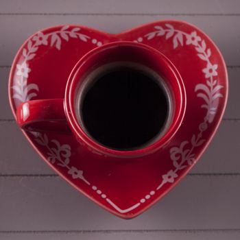 Red coffee cup over heart shaped plate (focus on the edge of the cup)