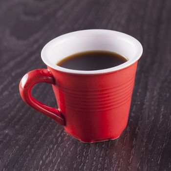 A small red cup of coffee over wooden background