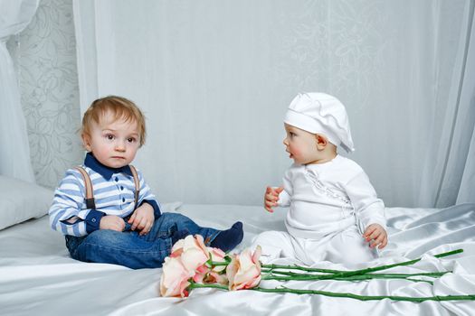 Cute brother and sister playing on a bed with silk sheets in the nursery
