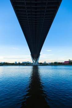 Bridge over a large river. Of surface reflects blue sky. Opposite side of the building in the city.