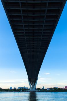 Bridge over a large river. Of surface reflects blue sky. Opposite side of the building in the city.