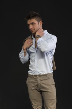 Handsome young man portrait, standing on dark background, with jacket on shoulder