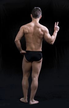 Back of muscular young man doing peace sign. Full length body shot on black