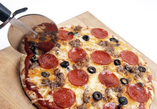 Pizza sits on a cutting board being sliced