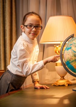 portret of little girl in eyeglasses pointing at globe