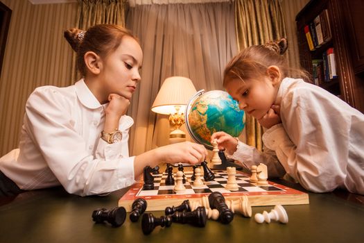 Portrait of two little sisters playing chess