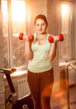 Portrait of young woman lifting dumbbells at fitness club at sunset