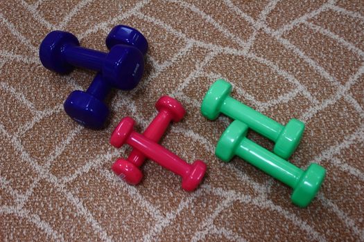 Colorful three pairs of dumbbells lying on the carpet for sports