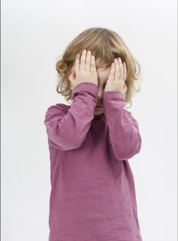 child covering eyes with hands. studio shot in grey background