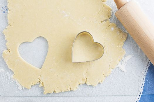 Heart shaped cookie cut out of cookie dough with cutter and rolling pin