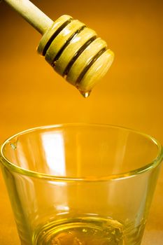 Honey drips off wood dipper into glass