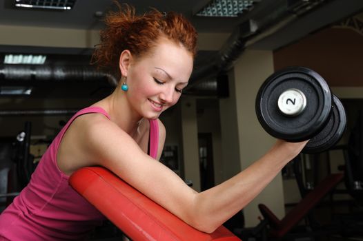 Young slim red haired girl doing biceps workout with dumbbell