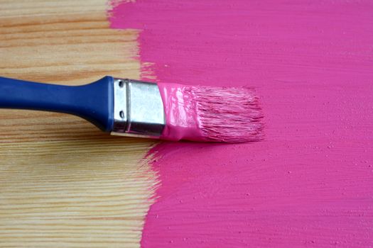 Pine board being painted pink with paintbrush