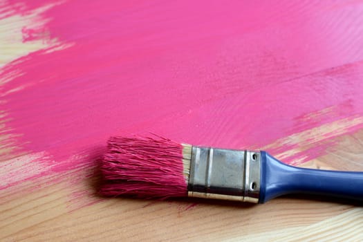 Paint-covered paintbrush on half-painted wooden board