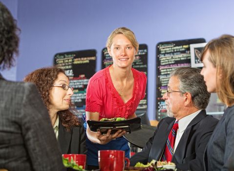 Pretty young server bringing food to group of business people