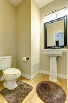 View of small bathroom with white toilet and washbasin stand. Hardwood floor with soft brown rugs