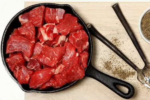 Raw Cubed Beef in Cast Iron Skillet on Table Top View.