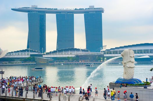 SINGAPORE - MAY 09, 2013: Tourists at the Merlion fountain in front of the Marina Bay Sands hotel in Singapore. Merlion is a imaginary creature with the head of a lion, seen as a symbol of Singapore