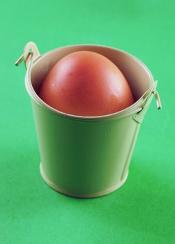 Egg in small bucket, over green background