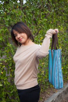 Portrait Asian woman Standing and holding a blue bag. Close to the bush and on the path in the park.