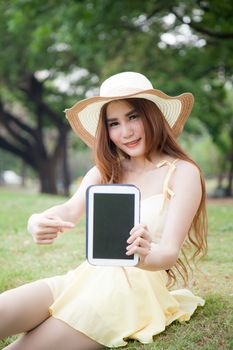 Asian women filed tablet and pointing to the tablet. She sitting on lawn in the park.