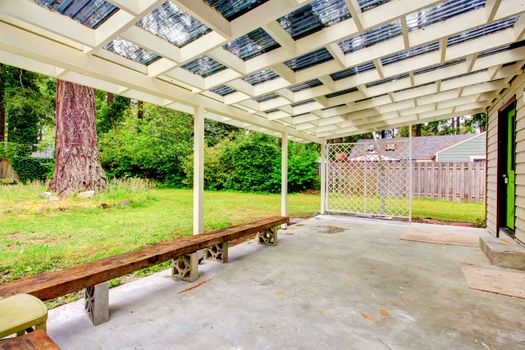 Backyard porch with concrete floor, wooden bench and chairs. View of nature landscape