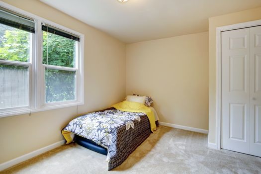 Small bedroom with window, carpet floor. View of mattress covered with floral bedding