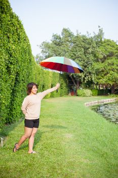 Asian woman holding an umbrella in the park. Stood on the lawn beside a tree.