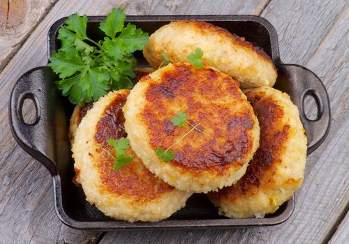 Delicious Chicken Meat Cutlets in Black Saucepan with Parsley isolated on Rustic Wooden background. Top View