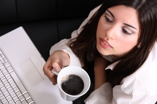 A young, hispanic adult girl watching a Laptop while drinking coffee.
