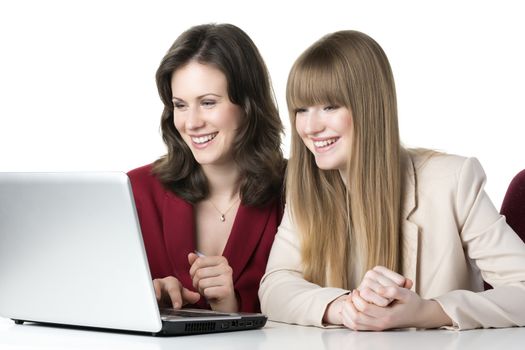 Two happy women blonde and brunette, sitting together in front of a laptop