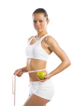 young athletic girl measuring waist measuring tape and holding a green apple, concept of healthy eating, isolated on white background