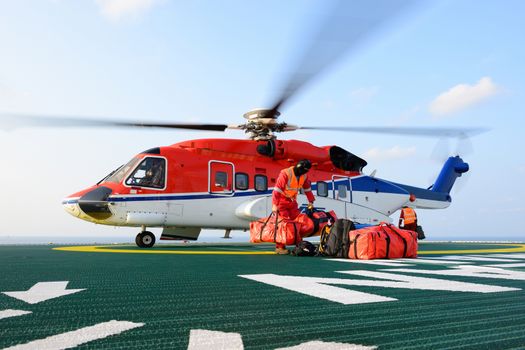 The helicopter landing officer loading baggage to helicopter at oil rig platform