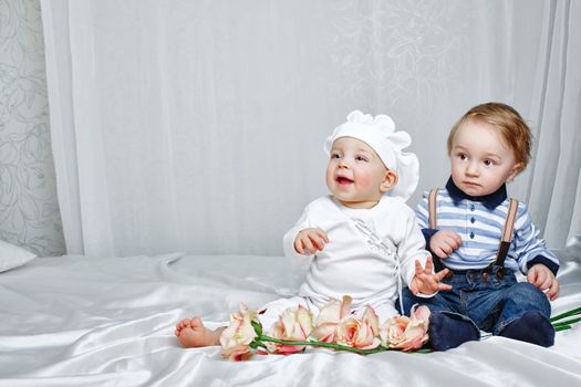 Cute brother and sister playing on a bed with silk sheets in the nursery