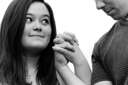 Young couple holding hands and showing the diamond engagement ring.  Shallow depth of field with sharpest focus on the ring. 