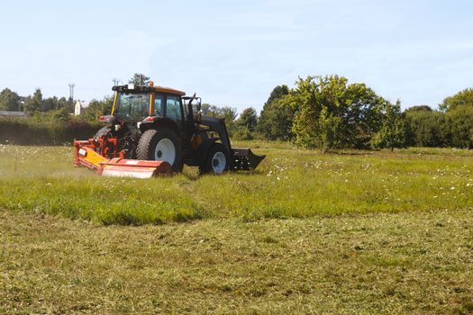 tractor mows the lawn in suburban field