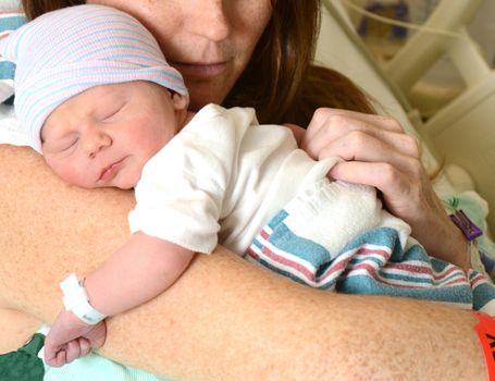new mother holding a sleeping newborn infant in hospital