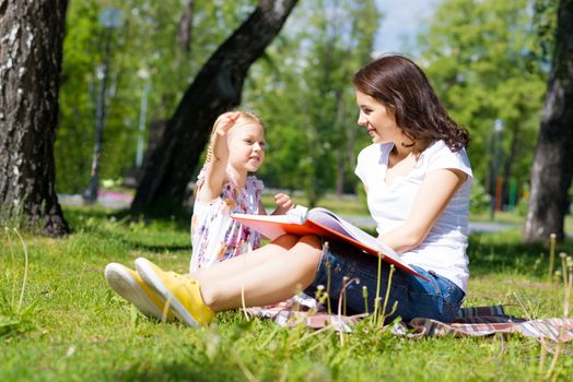 girl with the teacher reading a book together in the summer park