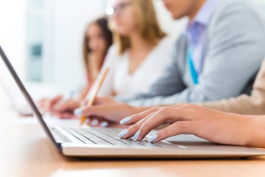 close-up of female hands on the laptop keyboard, students listen to the teacher at the University of